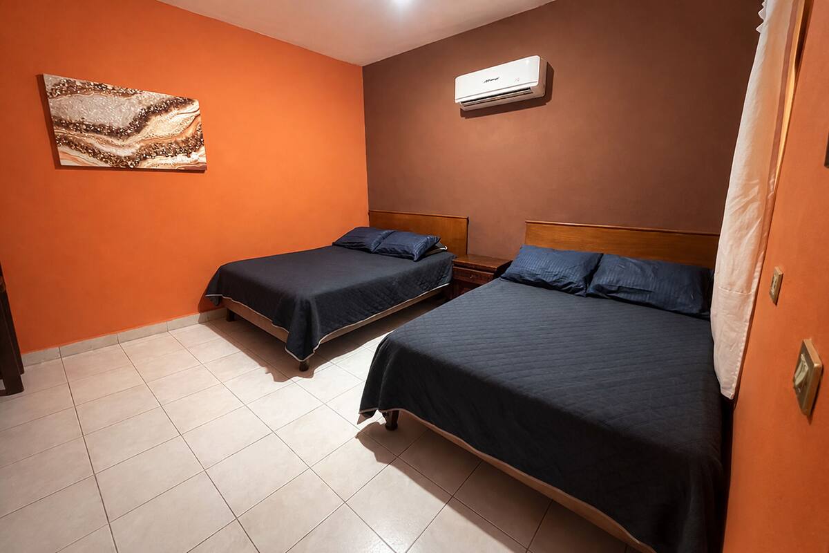 A room with two beds, an air conditioning unit, and a wall-mounted artwork.