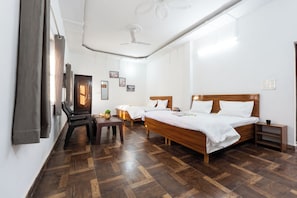 Une chambre d’hôtel avec un lit en bois, un bureau, une chaise, une petite table avec une plante et un ventilateur de plafond.