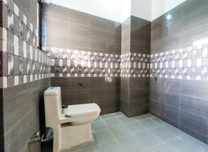 Une salle de bain avec des toilettes, une douche et des murs carrelés.