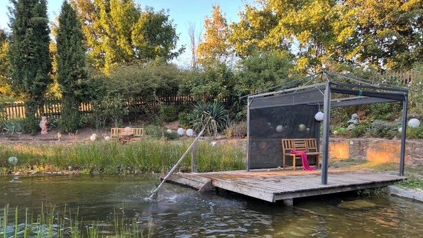 A wooden deck over a pond with a covered seating area and a chair.