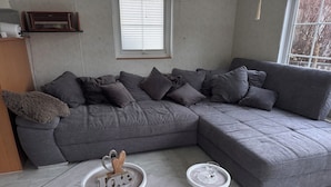 A modern living room with a grey sectional sofa, a small white side table, and a round white table with a glass on it.