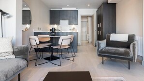 A modern living room with a grey sofa, a dark armchair, and a dining area with a table and chairs. - Montague Street (Dublin)