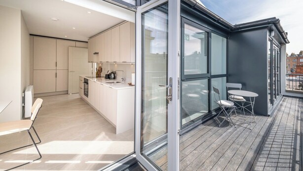 A modern kitchen with a large island, a dining area with a table and chairs, and a balcony with a table and chairs. - Montague Street (Dublin)