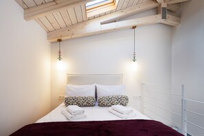 Ein Schlafzimmer mit Dachfenster, einem Bett mit gemusterten Textilien und zwei Wandleuchten.