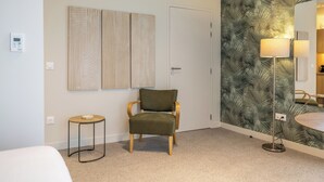 A hotel room with a bed, a green upholstered chair, a small round table, a floor lamp, and a wall with a leaf-patterned wallpaper. - Le Pic Coliving (Clermont-Ferrand)