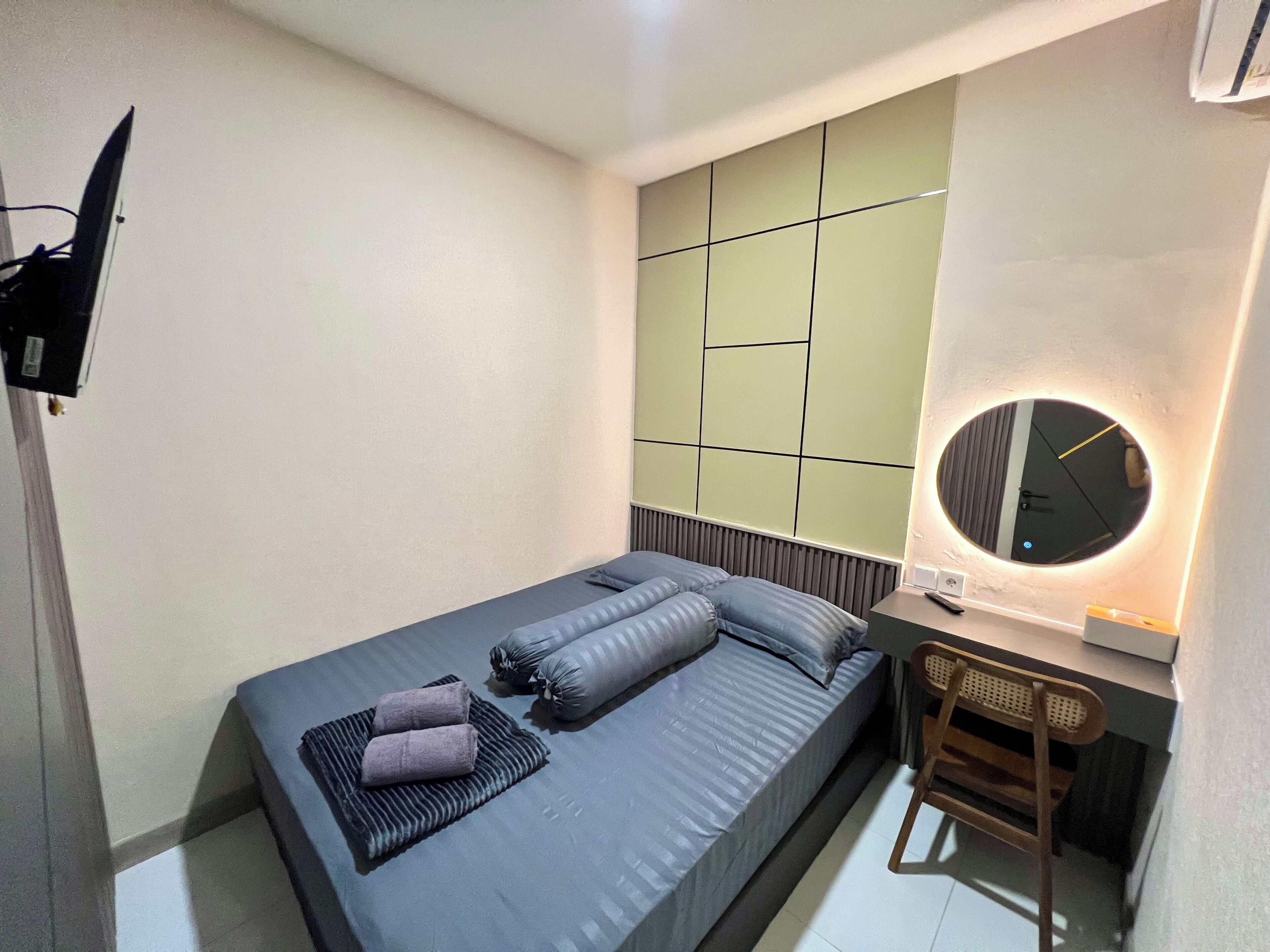 Ein modernes Hotelzimmer mit Bett, Nachttisch, Sessel und einem an der Wand befestigten Fernseher.