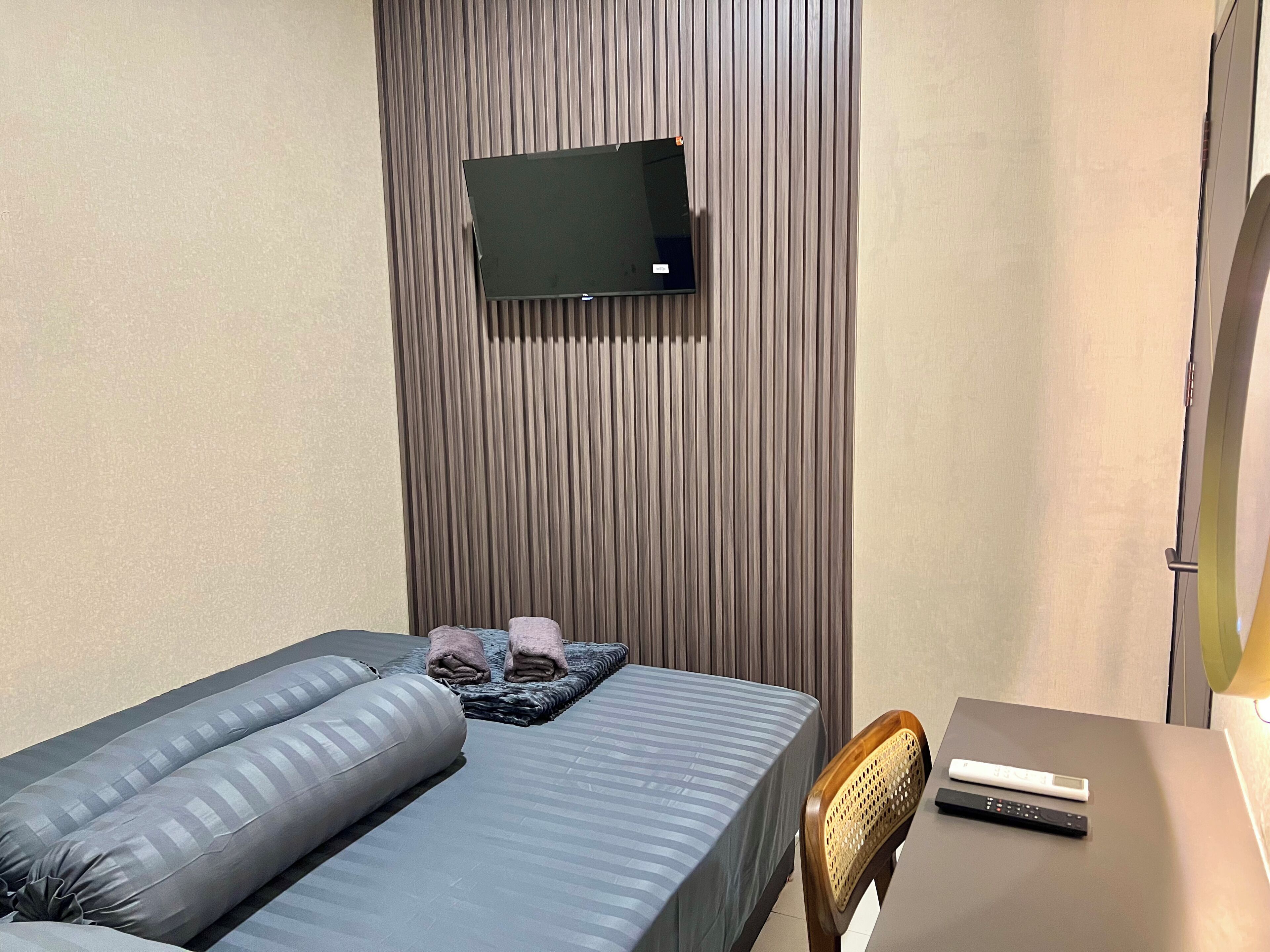 A hotel room with a bed, a desk, a chair, a television mounted on the wall, and a window.