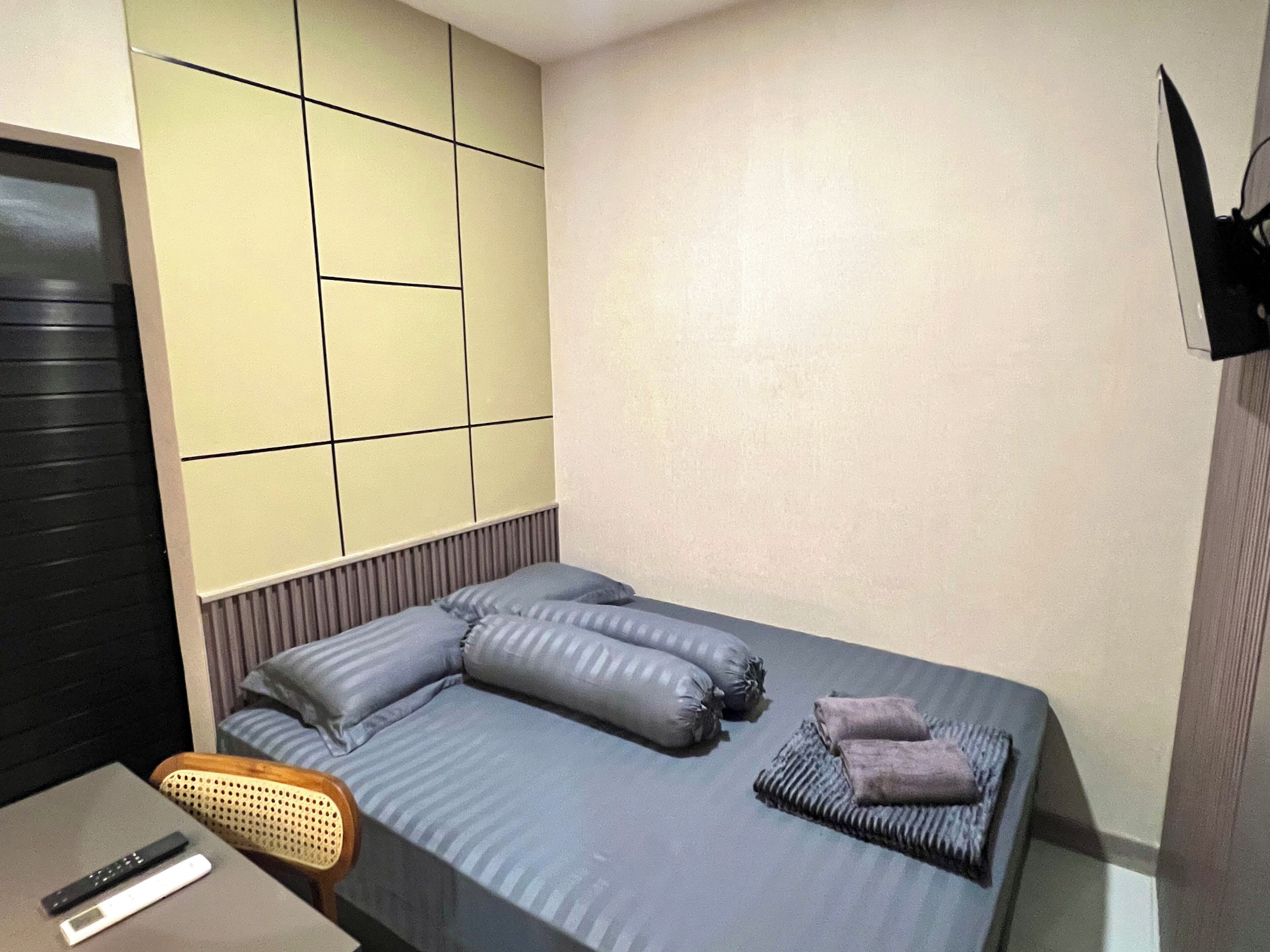 A hotel room with a bed, a chair, a TV, and a desk with a remote control.