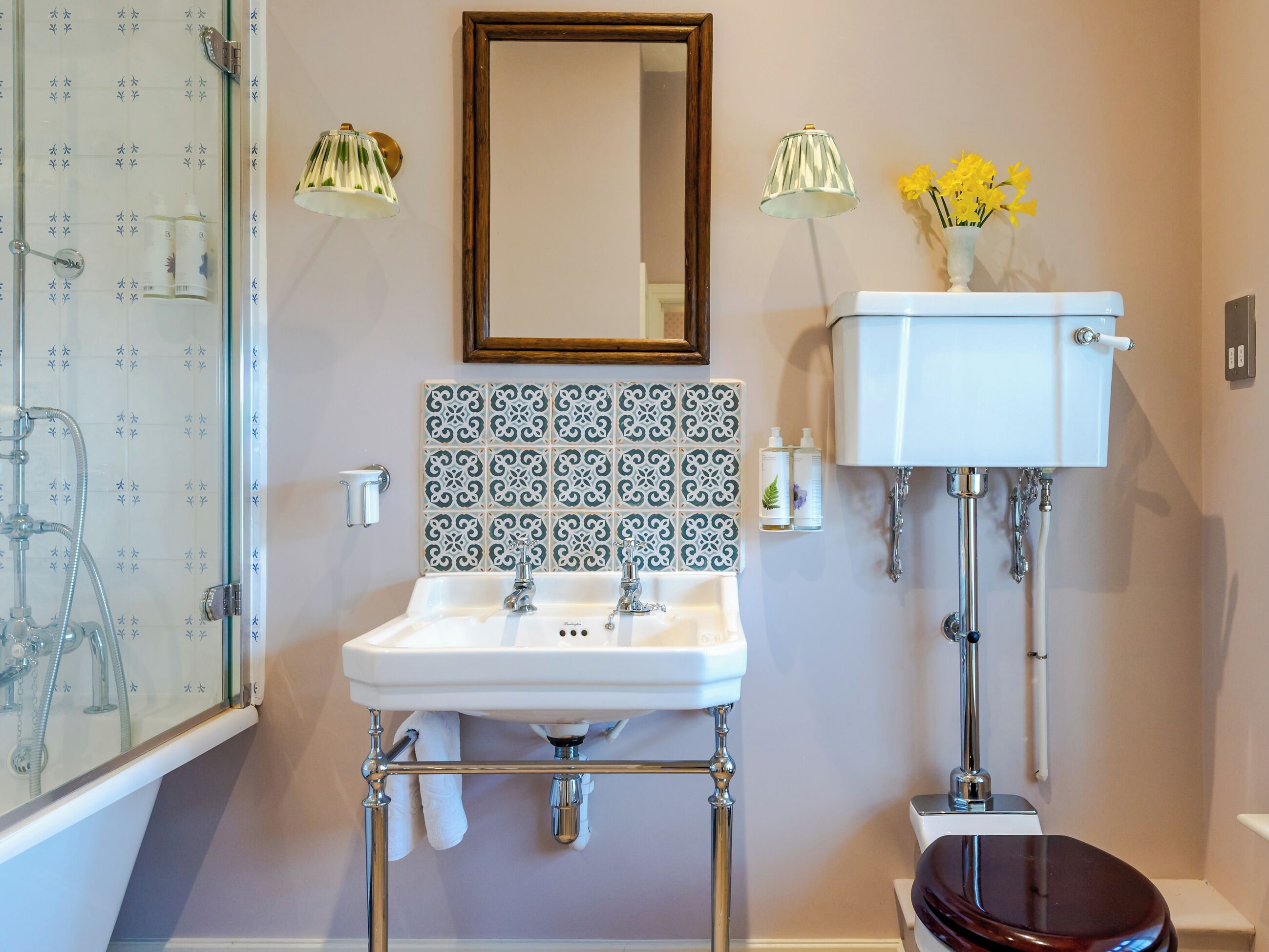 A bathroom with a white sink, two faucets, a mirror, a toilet, and a shower with a glass door.