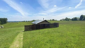 A rural landscape with a single building, a fenced area, and a clear sky.