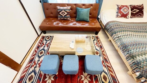 Een knus ingerichte kamer met een bruine leren bank, een klein houten tafeltje en blauwe zachte stoelen.