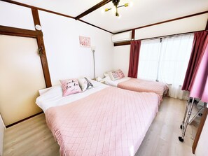 A hotel room with two beds, a ceiling fan, a window with curtains, and a radiator. - Honmachi 1 Chome (Tokyo)