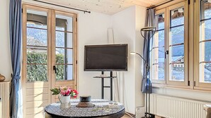 Um quarto aconchegante com uma mesa redonda, uma TV de tela plana e janelas amplas que oferecem vista para o exterior.