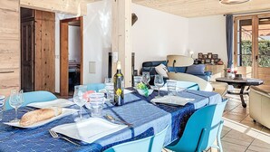 Uma área de refeições com uma mesa posta para dois, com toalha de mesa azul estampada, cadeiras e diversos utensílios de mesa.
