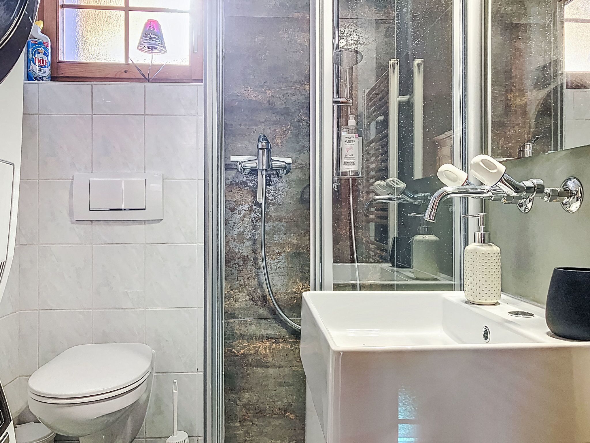 Une salle de bain comprenant des toilettes, une douche avec une porte en verre et un lavabo avec un distributeur de savon.