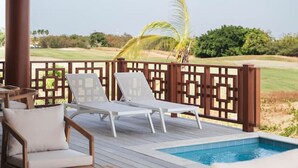 Ein überdachter Außenbereich mit Pool, Liegestühlen und Blick auf einen Golfplatz.