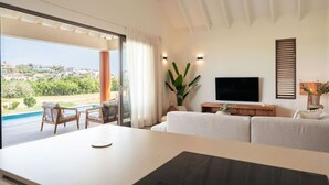 Ein modernes Wohnzimmer mit großem Fernseher, einer Couch, einem Esstisch und Blick auf einen Pool und die Landschaft.