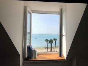 Blick aus einem Fenster mit Holzboden, einem Bücherregal mit Büchern und einem klaren Himmel.