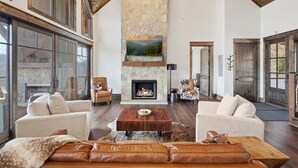Ein geräumiges Wohnzimmer mit Kamin aus Stein, Ledersofas und großen Fenstern.