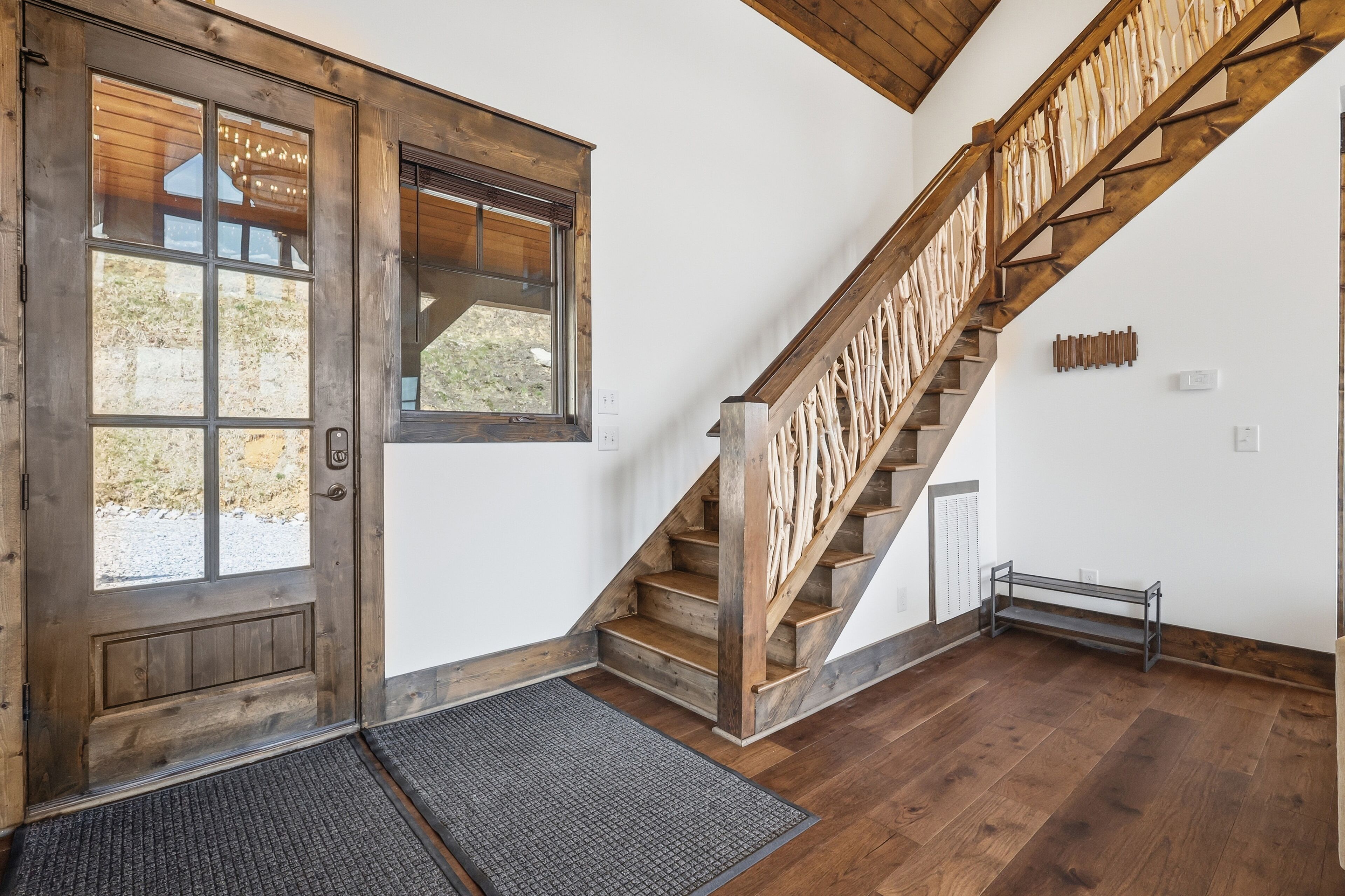 A wooden staircase with a metal handrail, a wooden door with glass panels, and a doormat.