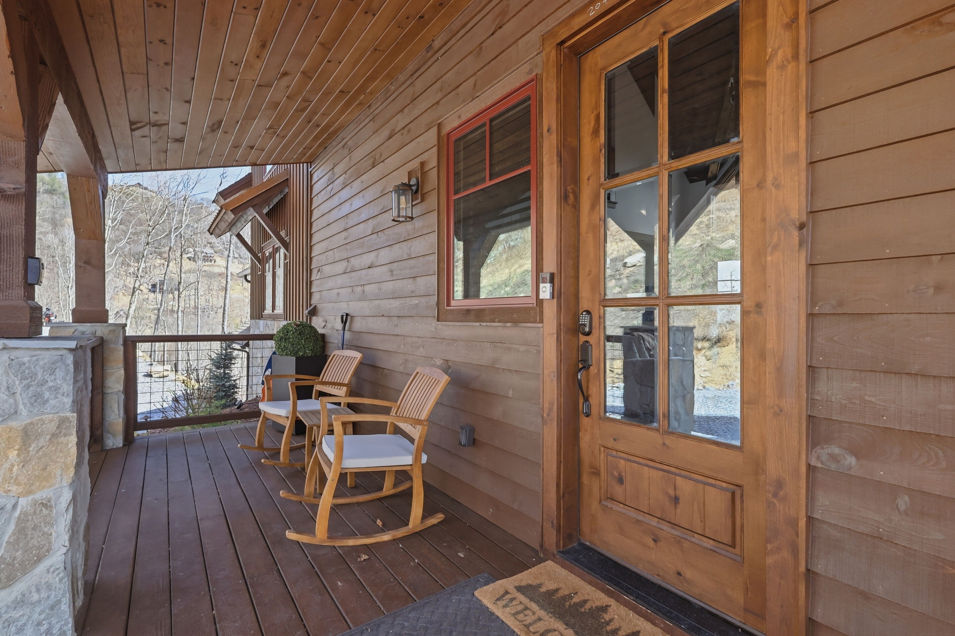 Un portico in legno con parete in pietra, una porta in legno con vetri e un tavolo con sedie.