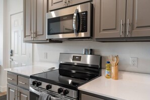 Una cocina moderna con electrodomésticos de acero inoxidable, incluyendo un microondas y un horno, y utensilios de madera sobre la encimera.