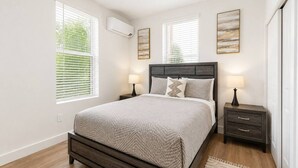 A bedroom with a bed, bedside tables, and artwork on the walls. - Modern 2BR Suite • Convention • Bathhouse Row (Hot Springs)