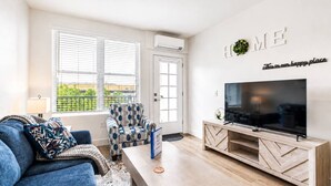 A modern living room with a sofa, armchair, coffee table, TV, and a wall-mounted sign. - Modern 2BR Suite • Convention • Bathhouse Row (Hot Springs)
