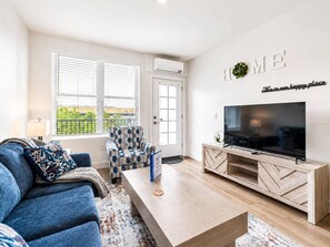 A modern living room with a sofa, armchair, coffee table, TV, and a wall-mounted sign. - Modern 2BR Suite • Convention • Bathhouse Row (Hot Springs)