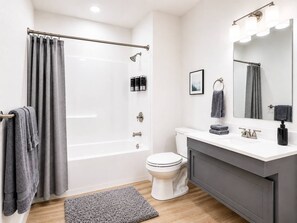 A modern bathroom with a bathtub, toilet, and vanity. - Modern 2BR Suite • Convention • Bathhouse Row (Hot Springs)