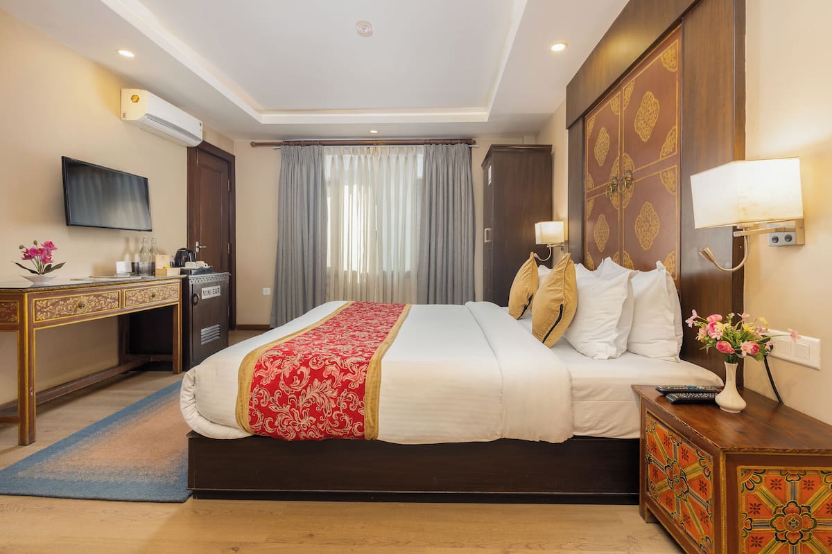 A hotel room with a large bed, a desk with a computer, a TV mounted on the wall, and a minibar.