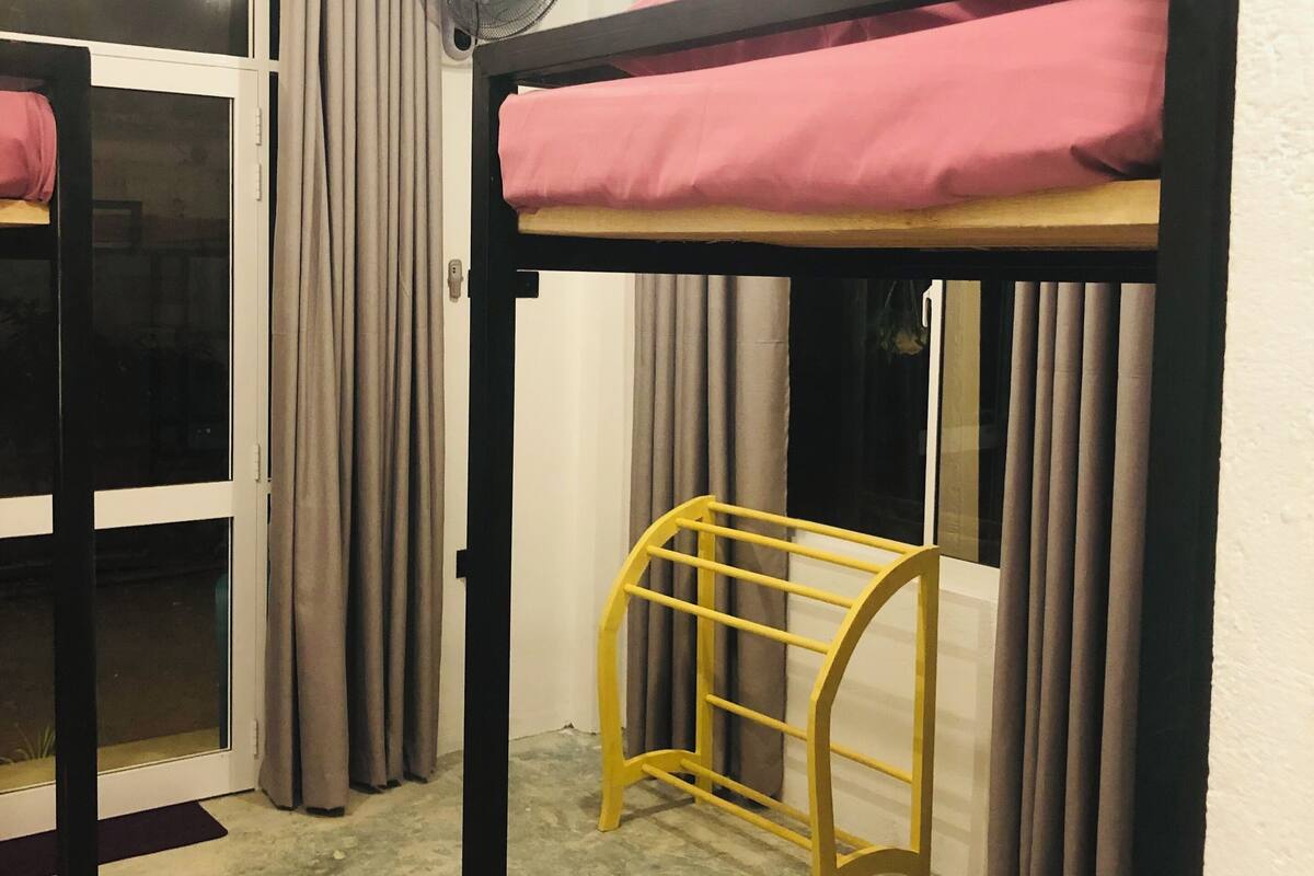 A bunk bed room with a fan, curtains, and a window.