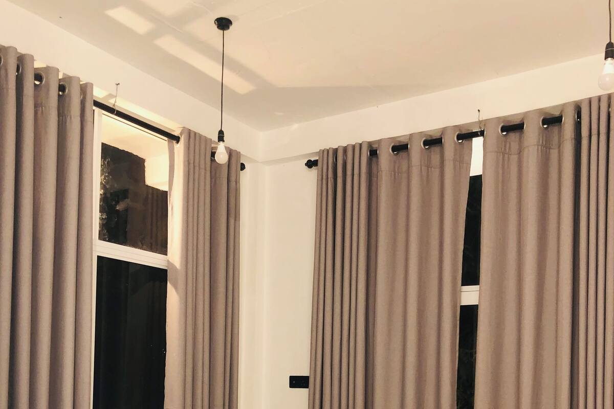 A bedroom with a bed, curtains, a window, and a light fixture.