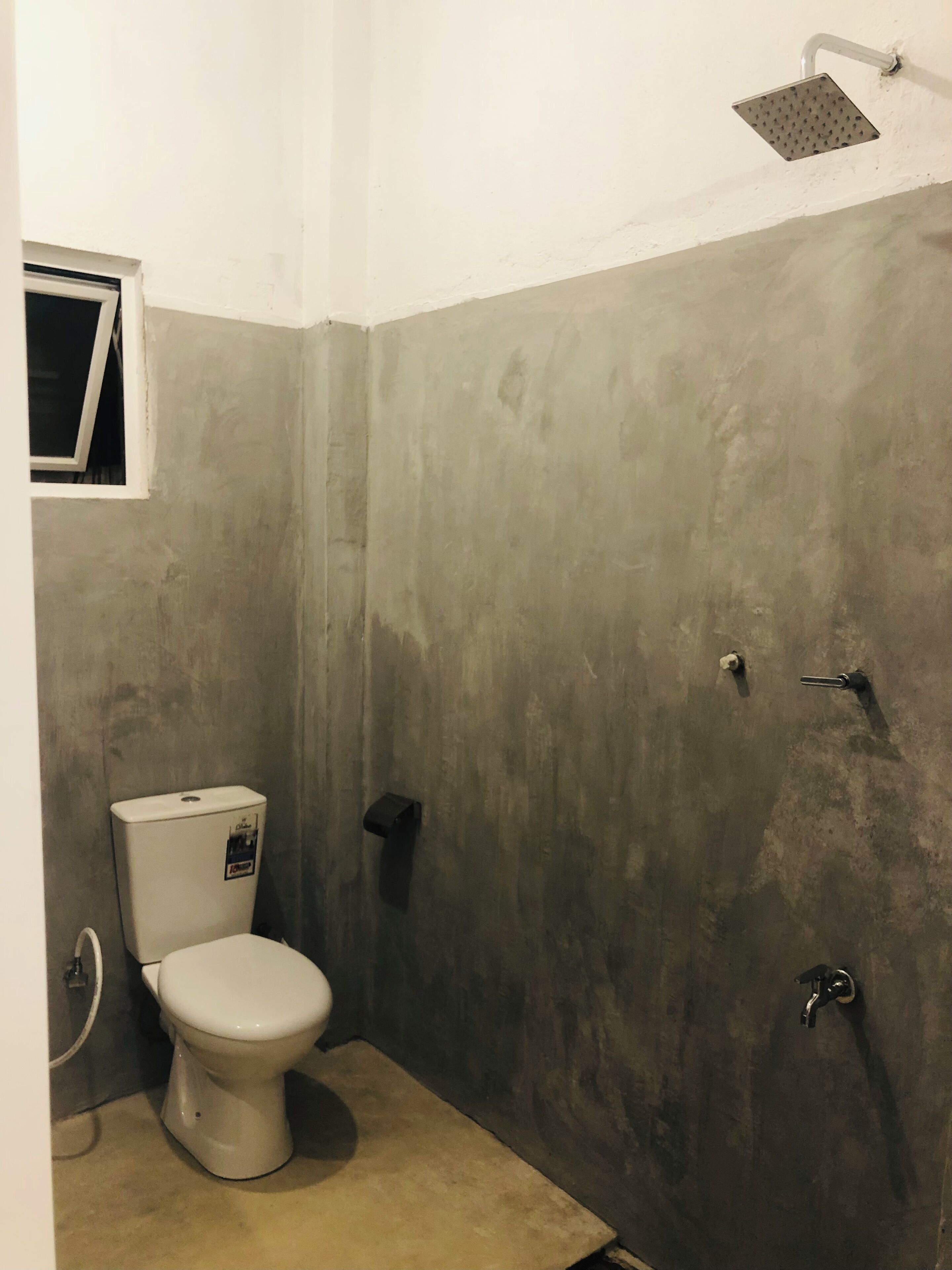 Une salle de bain avec des toilettes, une douche et une petite fenêtre.