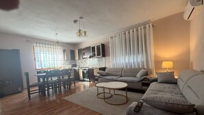 A modern living room with a sofa, a dining table, and a kitchen area.