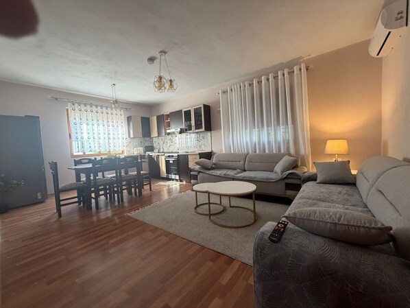 A modern living room with a sofa, a dining table, and a kitchen area.