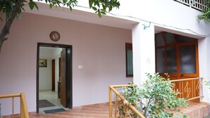 A building entrance with a wooden door, a small balcony with a railing, and a tiled floor.