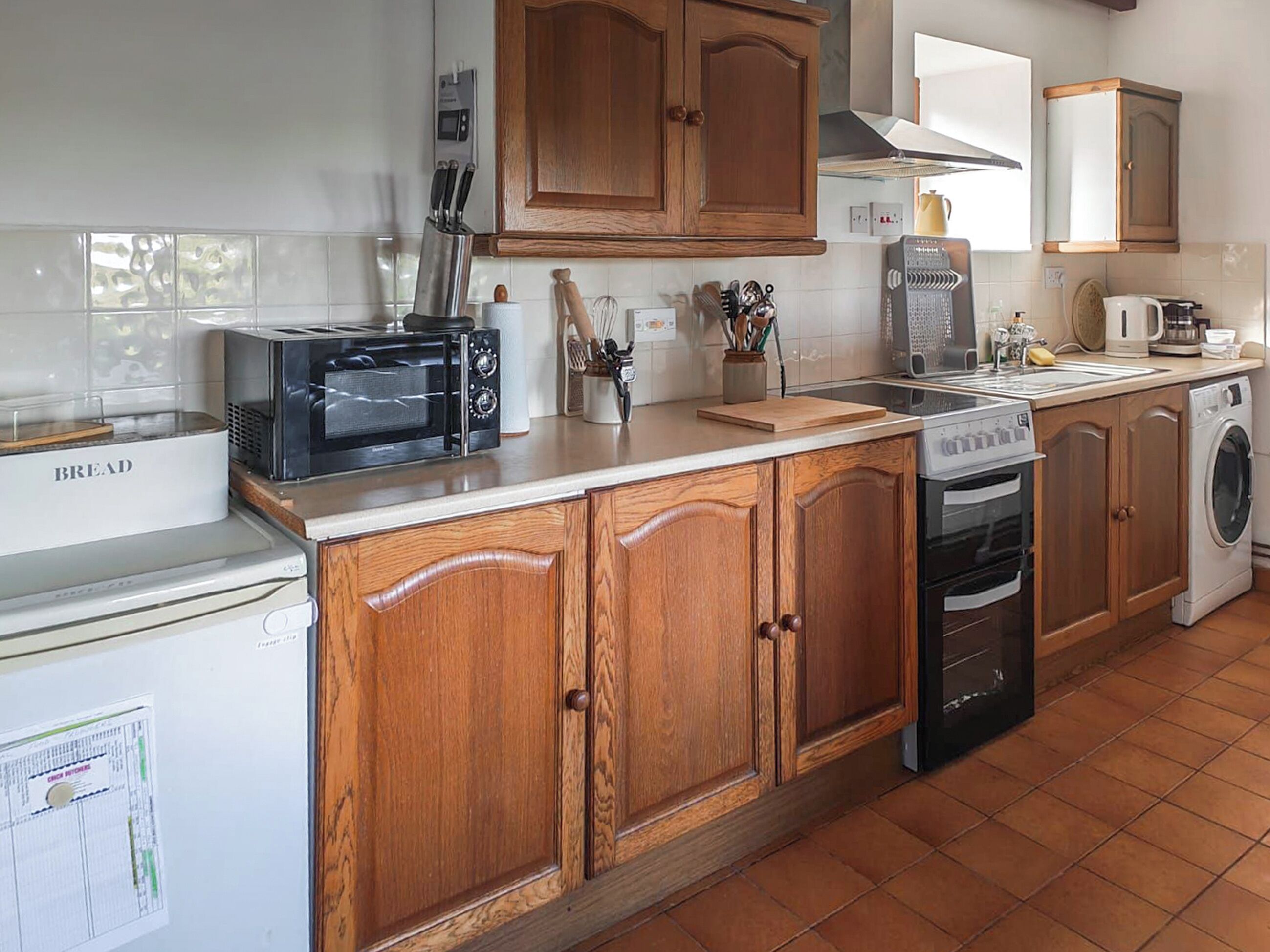 Una cocina con armarios de madera, un panificadora, un tostador, un microondas, una cafetera y una lavadora.