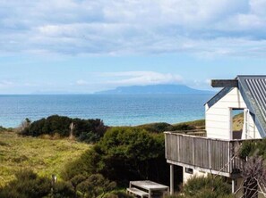 A coastal property with a white building featuring a balcony, overlooking the sea and a distant mountain. - Pakiri Beachhouse  Retreat and Relax (Tomarata)