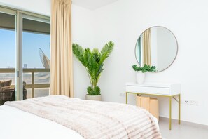 A bedroom with a bed, a white vanity, a mirror, a potted plant, and a view through a sliding glass door. - Bloomfields 1BR in Ajwan Towers - Saadiyat (Abu Dhabi)