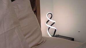 Una cama con una almohada blanca y una lámpara de noche de diseño moderno con forma de espiral.