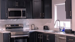 Una cocina moderna con gabinetes oscuros, electrodomésticos de acero inoxidable, horno empotrado y pileta.