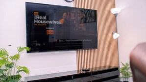 Televisor de pantalla plana montado en la pared mostrando 'The Real Housewives of Atlanta', temperatura de 11°C y hora 1:19 p.