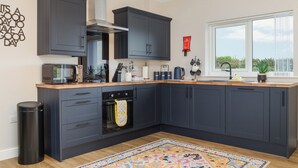Une cuisine moderne avec des meubles de couleur sombre, un four encastré, un four à micro-ondes et une grande fenêtre offrant une vue dégagée.