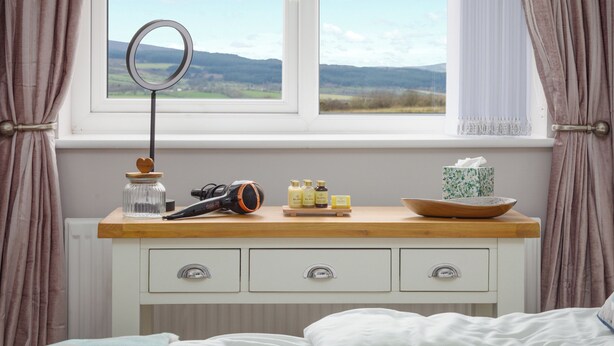 Une chambre à coucher avec une commode en bois, un miroir et une fenêtre donnant sur des collines.
