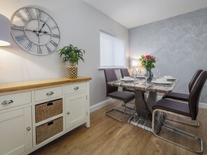 Un coin repas avec une table en bois, des chaises, une horloge, une plante en pot et un vase rempli de fleurs.