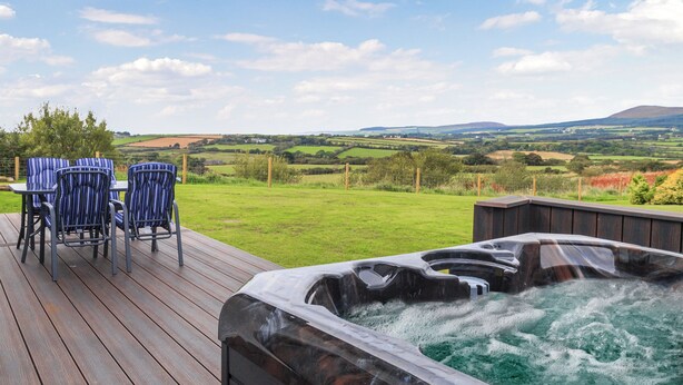 A hot tub on a wooden deck with chairs, overlooking a green landscape.