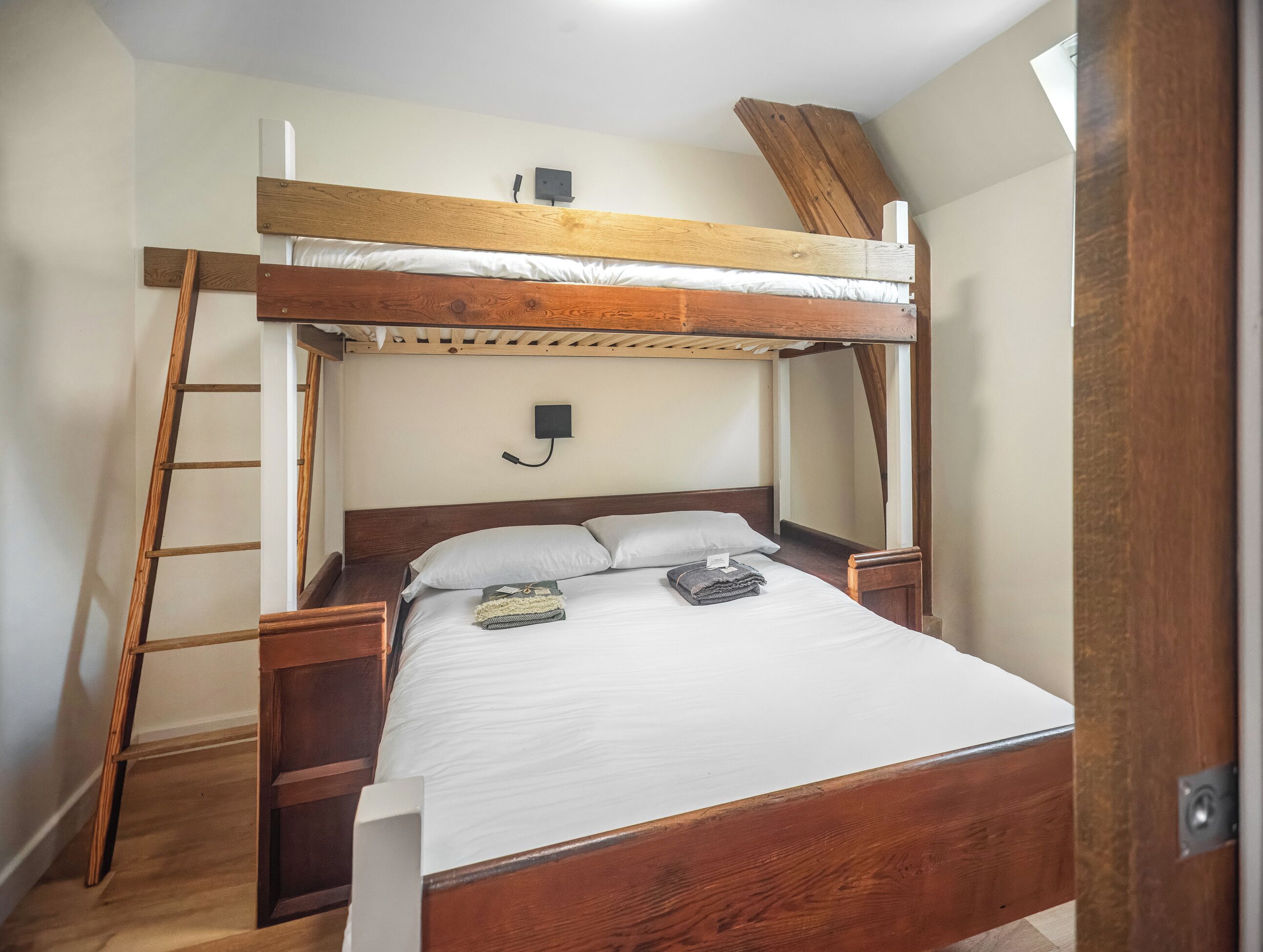 Un lit superposé avec une échelle en bois, une table de chevet et un luminaire fixé au mur.