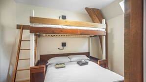Una cama litera con escalera de madera, una mesita de noche y una lámpara fijada a la pared.