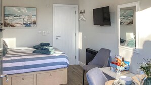 Un dormitorio con cama, una silla, una mesa con un bol y una copa de vino, y un televisor en la pared.